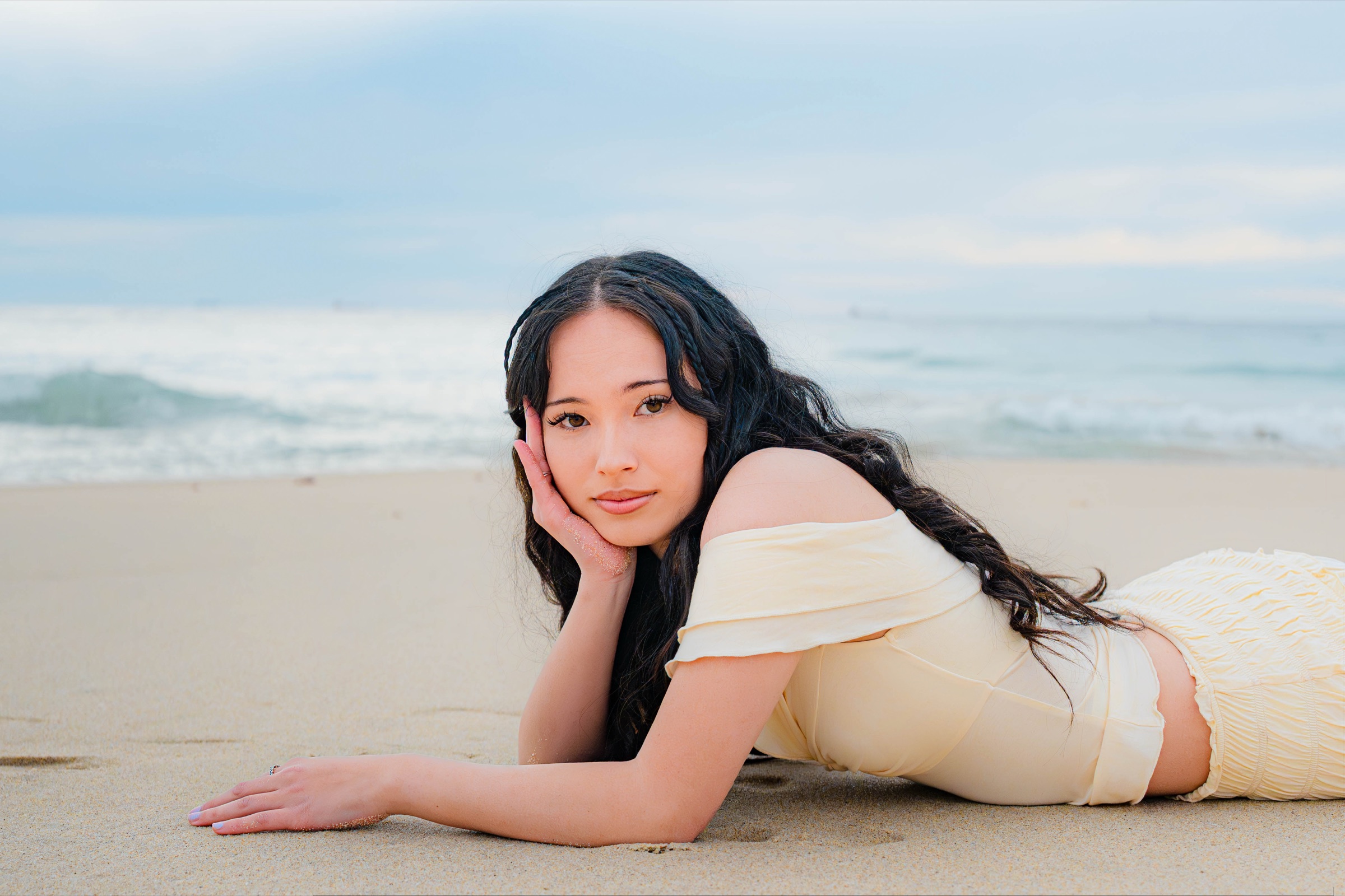 Woman in cream lying on the sand with the ocean behind her