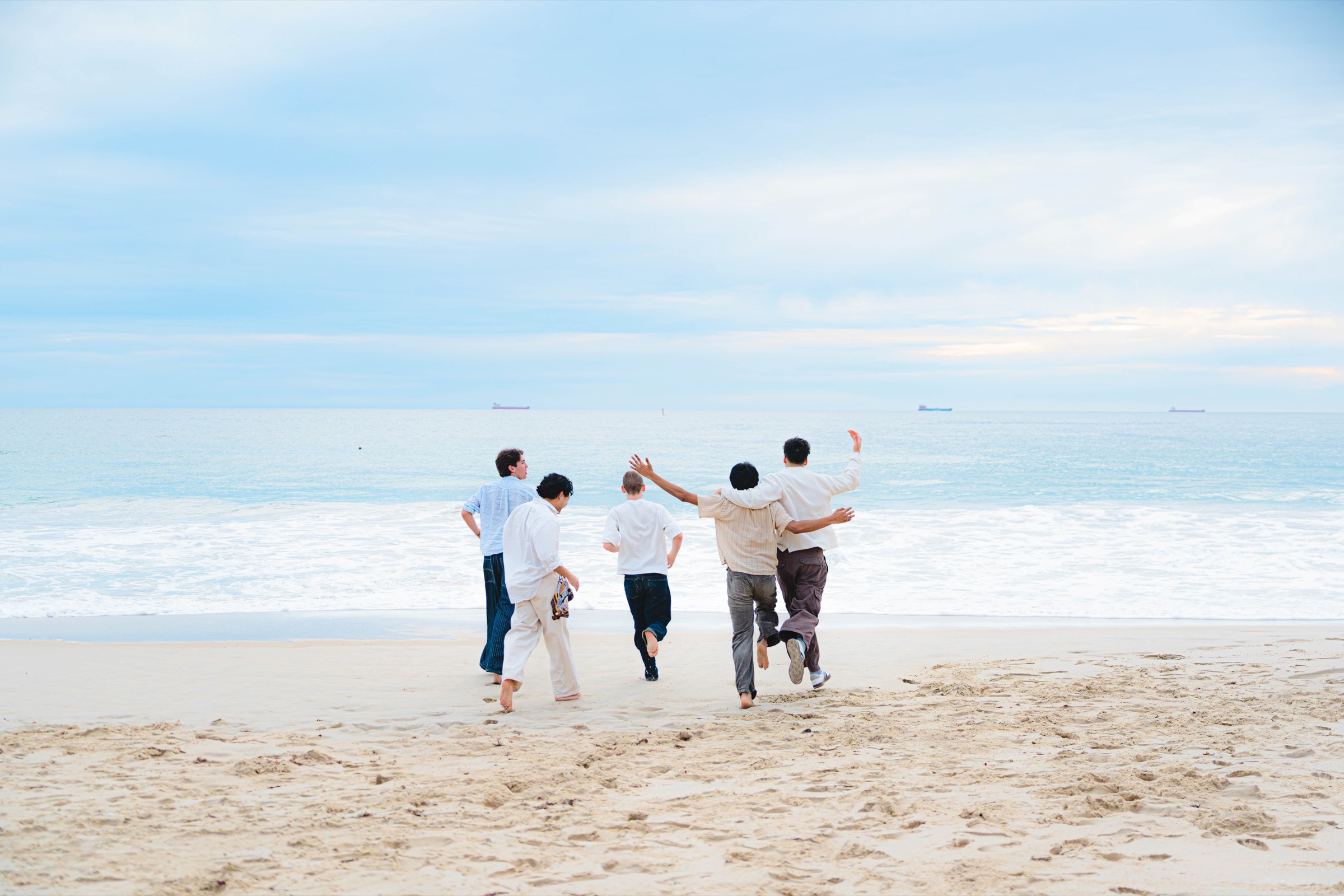 Group of friends running toward foamy ocean waves