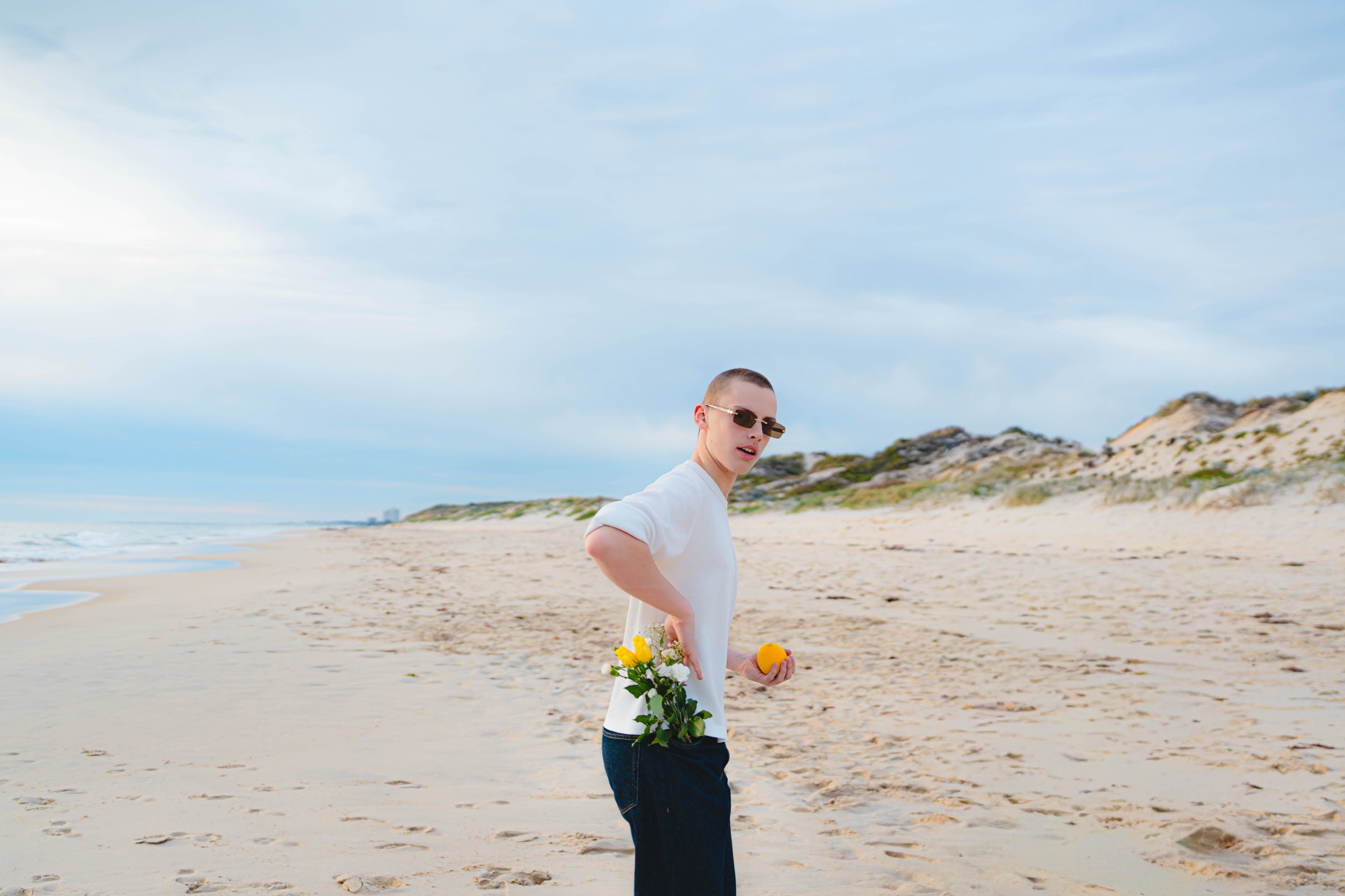 Man holding yellow flowers and a lemon on a quiet beach