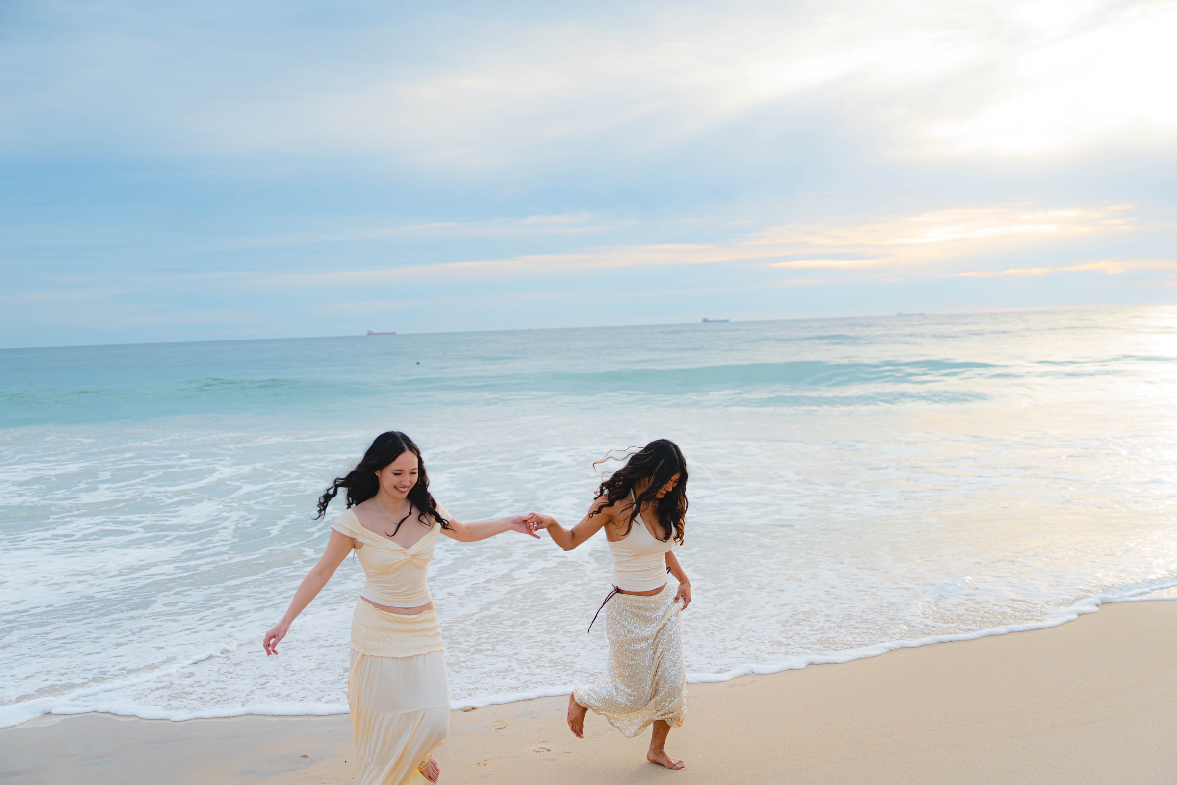 Two women walking hand in hand along the shoreline at sunset