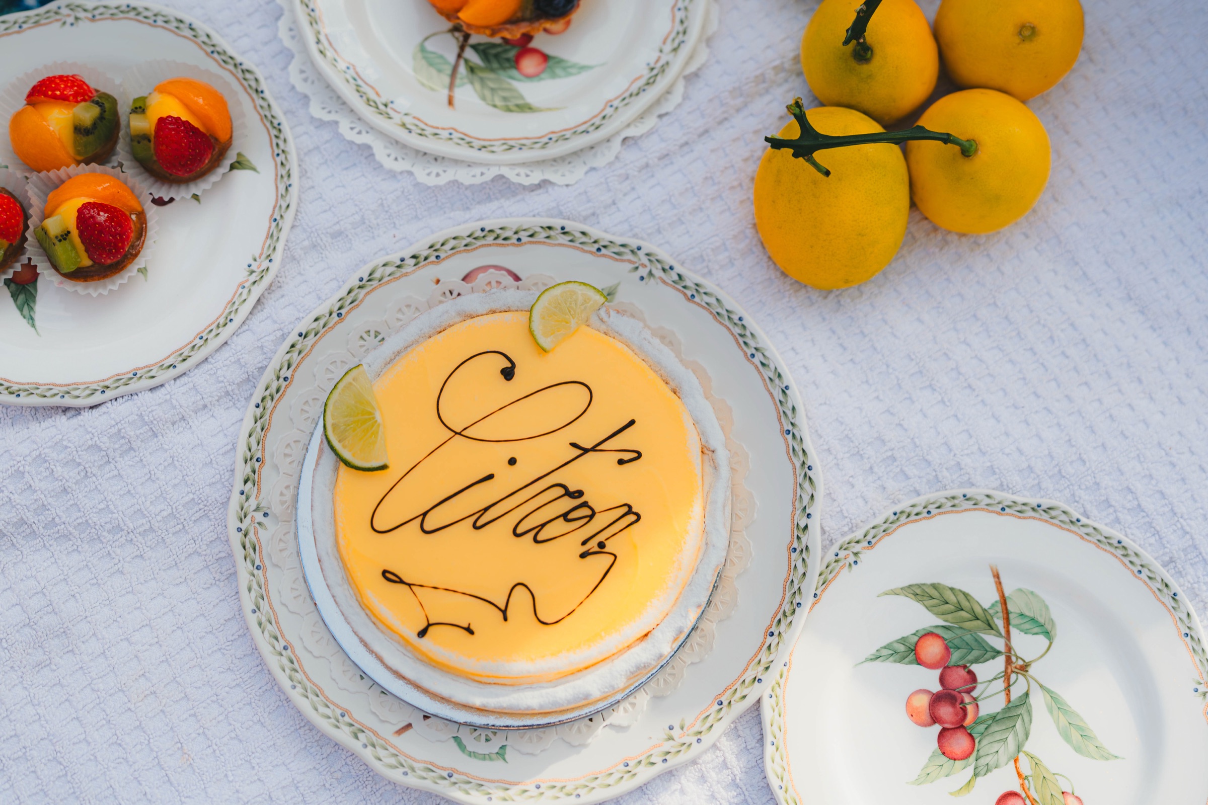 Lemon cake, fruit tarts, and fresh lemons arranged on patterned plates