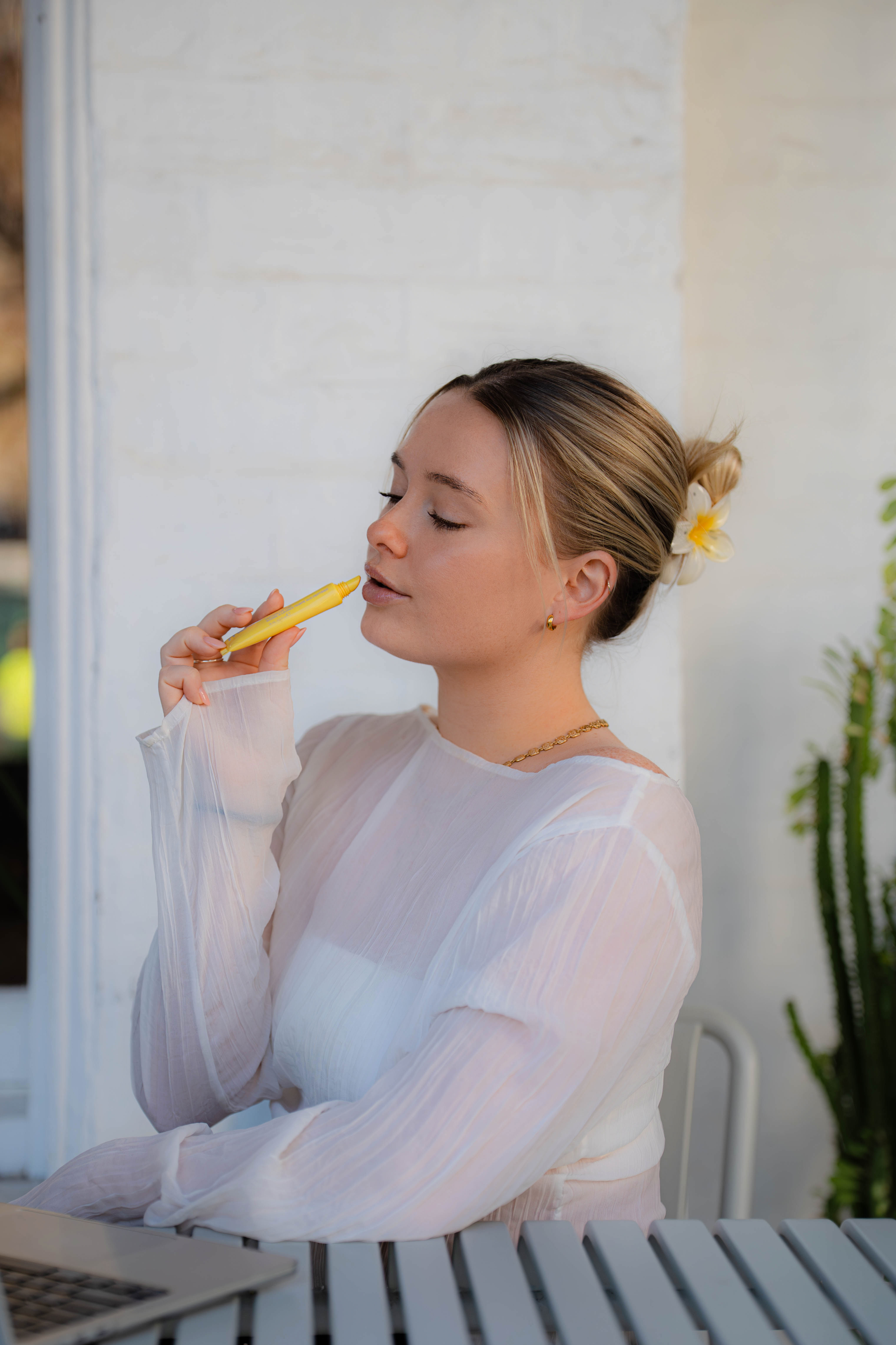 Woman applying yellow lip balm on a sunlit terrace