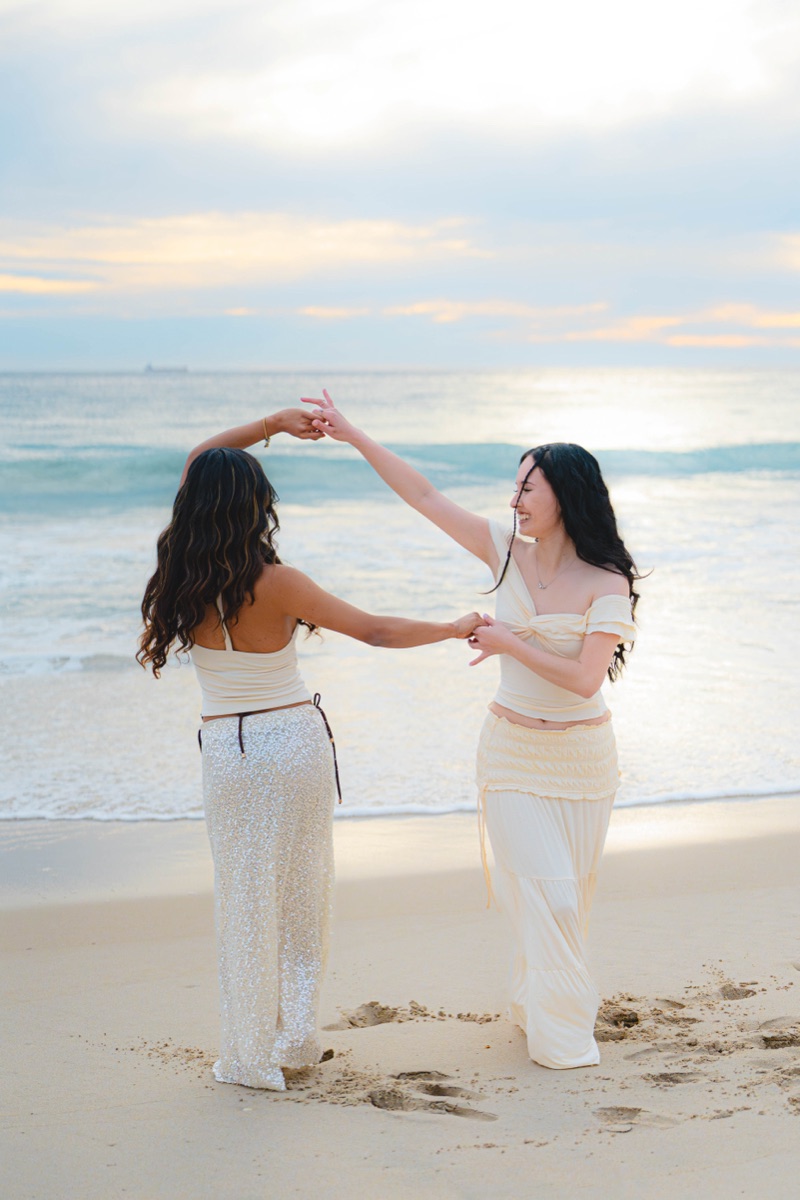 Two women dancing by the ocean at sunset