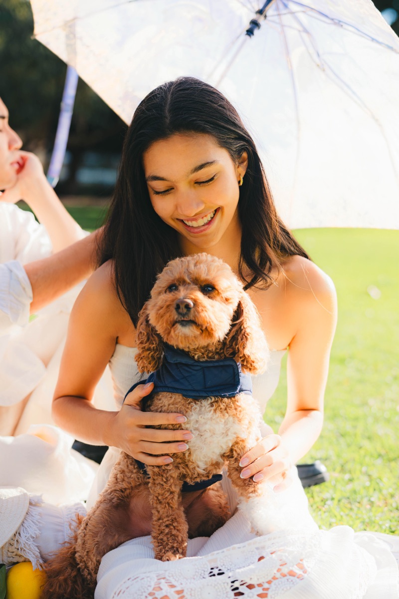 Woman smiling while holding a small dog under a white umbrella